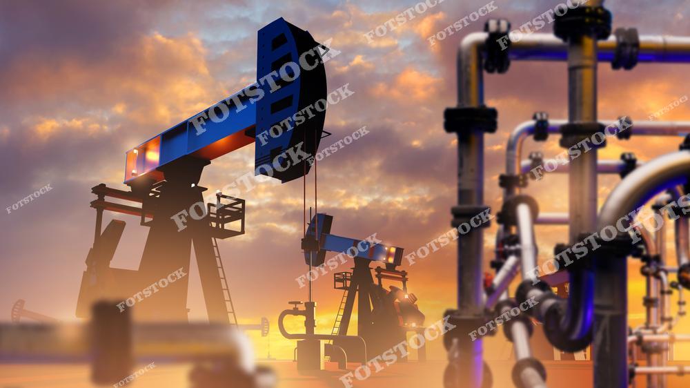 Силуэты нефтяных качалок на фоне заката с видимыми трубопроводами на переднем плане. Фотография отражает процесс добычи и транспортировки нефти, подчеркивая инфраструктуру энергетического сектора и её роль в обеспечении топливными ресурсами.
